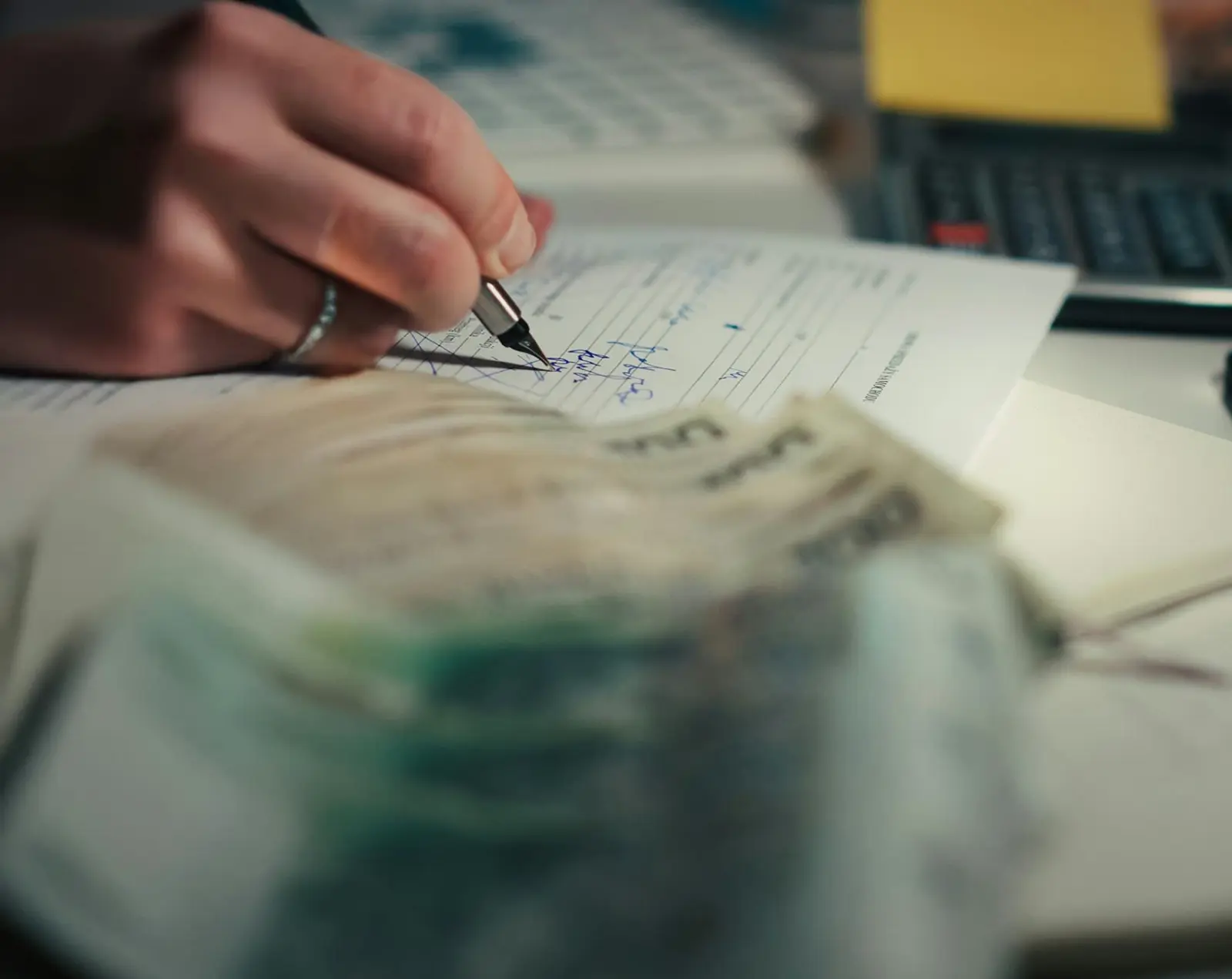 A hand writing figures into a notebook beside cash and a calculator, working out a wedding budget